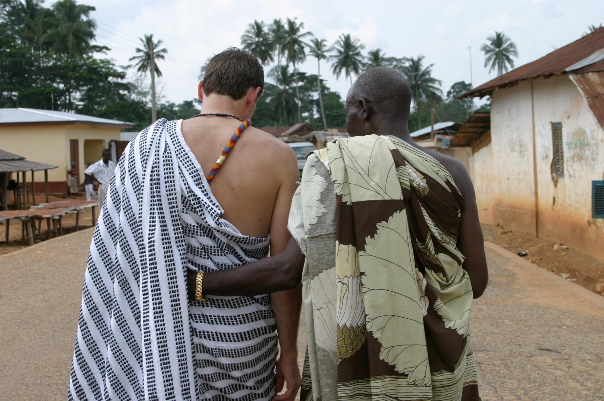 A HART volunteer and Ghanaian community leader walking arm in arm in traditional cloth